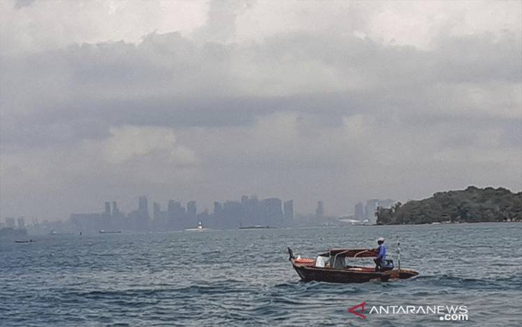 Seorang warga Kota Batam berlayar di sekitar Perairan Belakangpadang, dengan latar gedung pencakar langit Singapura, beberapa waktu lalu. (ANTARA/Naim)