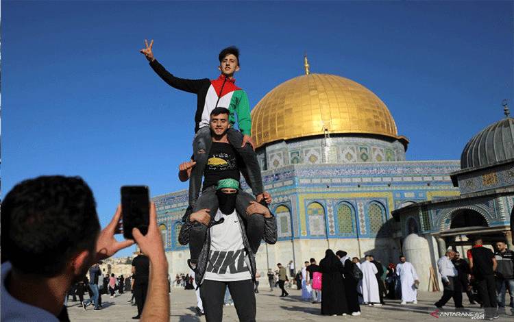 Seorang pemuda Palestina memotret rekannya yang berpose dengan latar belakang Dome of the Rock setelah shalat Idul Fitri 1442 H, di akhir bulan suci Ramadhan, di kompleks masjid al-Aqsa, yang dikenal umat Muslim sebagai Tempat Suci dan Yahudi sebagai Temple Mount, di Kota Tua Yerusalem, di tengah pertempuran Israel-Gaza, Kamis (13/5/2021). ANTARA FOTO/Reuters-Ammar Awad/hp