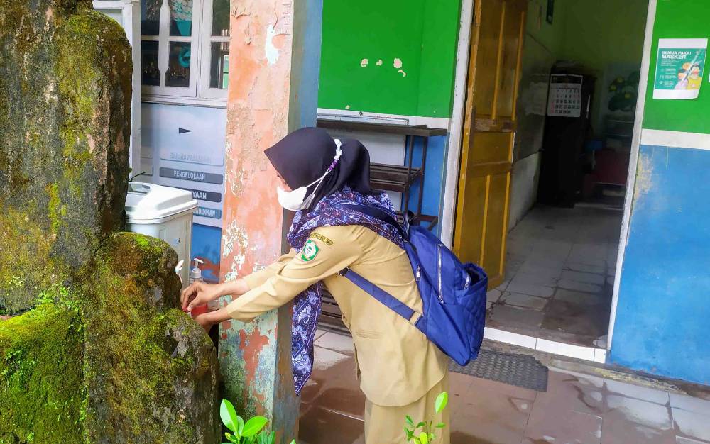 Seorang guru mencuci tangan sebelum memasuki lingkungan sekolah.