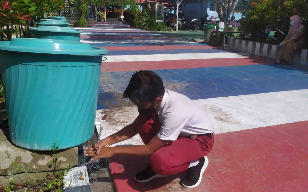 Seorang siswa mencuci tangan ketika memasuki lingkungan sekolah.