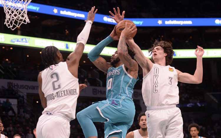 Forward Charlotte Hornets Miles Bridges (tengah) hendak menembakkan bola melewati hadangan guard Oklahoma City Thunder Shai Gilgeous-Alexander (kiri) dan lulusan Josh Giddey (kanan) pada babak kedua di The Spectrum Center, Charlotte, AS, Jumat (21/1/2022)