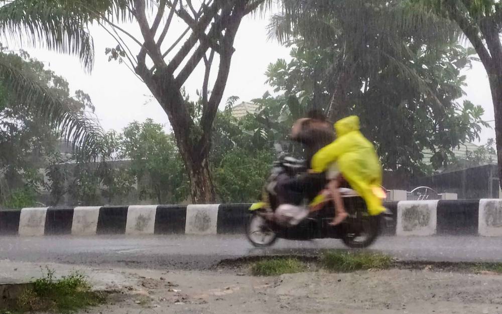 Pengendara motor melintasi jalan yang diguyur hujan di Sampit.