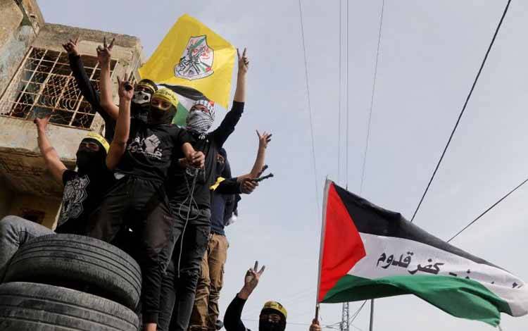 Pengunjuk rasa asal Palestina mengangkat tangan mereka saat mereka membawa bendera Fatah dan Palestina di tengah bentrok dengan pasukan Israel saat protes memperingati Hari Tanah (Land Day), di Kafr Qaddum di Tepi Barat, Jumat (1/4/2022)