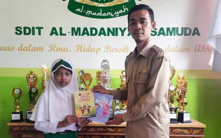 Dira Khairunna Latifa Marsudi, menyerahkan buku karya tulisnya kepada Kepala SDIT Al-Madaniyah, Mutaqin Saufi
