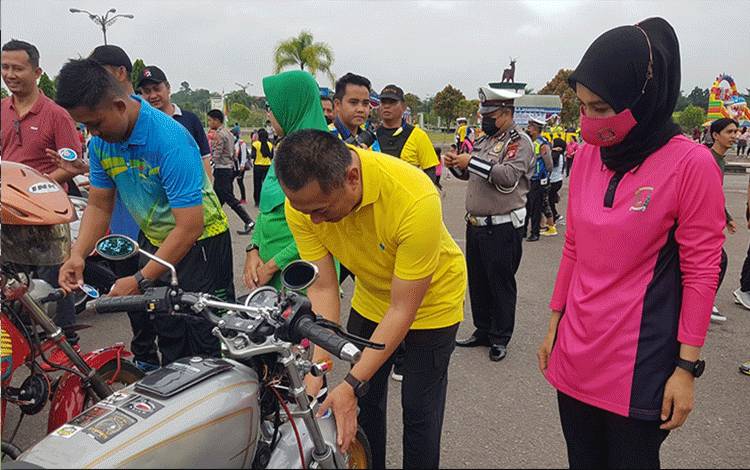 Kapolres Lamandau AKBP Bronto Budiyono menempelkan stiker HUT Satlantas Ke-76 di salah satu kendaraan milik anggota komunitas motor di lamandau. (FOTO : HENDI NURFALAH)