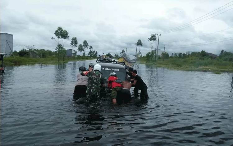 Babinsa Koramil 1014 - 01/Arut Selatan bersama instansi terkait dan warga membantu evakuasi mobil pikap terjebak banjir.