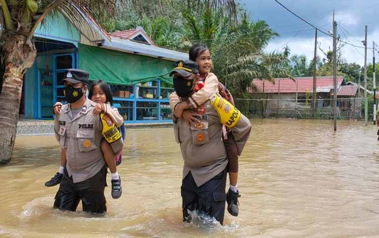 Kapolsek Aruta Ipda Agung Sugiarto bersama anggota menggendong pelajar saat berangkat se kalah melintasi banjir. (FOTO : POLSEK ARUTA)