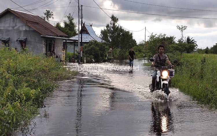Pengendara melintasi jalan yang tergenang, Rabu, 19 Oktober 2022. (FOTO: NORHASANAH)