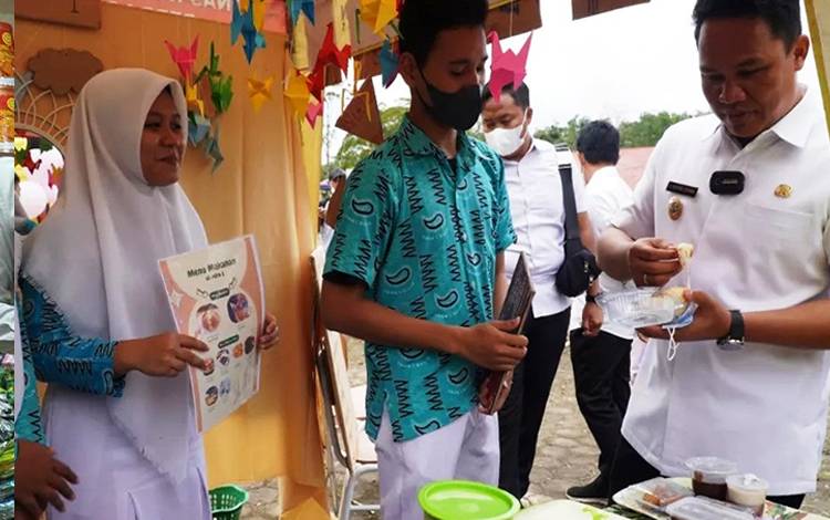 Bupati Lamandau Hendra Lesmana menyambangi dan mencicipi makanan yang ditawarkan salah satu siswa SMAN 1 Bulik. (FOTO : HENDI NURFALAH)