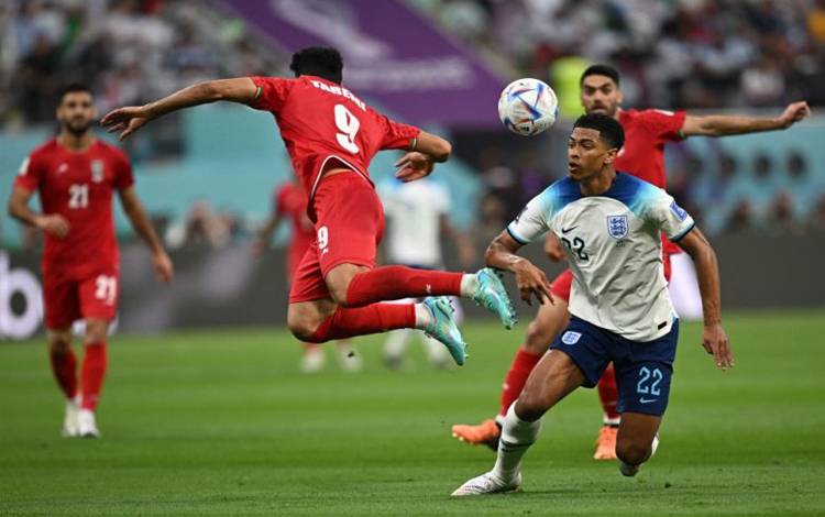 Striker Iran Mehdi Teremi #9 (tengah) menyundul bola di samping gelandang Inggris #22 Jude Bellingham pada laga pembuka Grup B antara Inggris melawan Iran di Stadion Internasional Khalifa, Doha. (21/11/2022) (AFP/PAUL ELLIS)