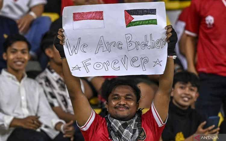 Seorang suporter Indonesia membawa poster bertuliskan dukungan untuk Palestina saat pertandingan FIFA matchday di Stadion Gelora Bung Tomo Surabaya, Rabu (14/6/2023) malam. (ANTARA FOTO/Muhammad Adimaja)