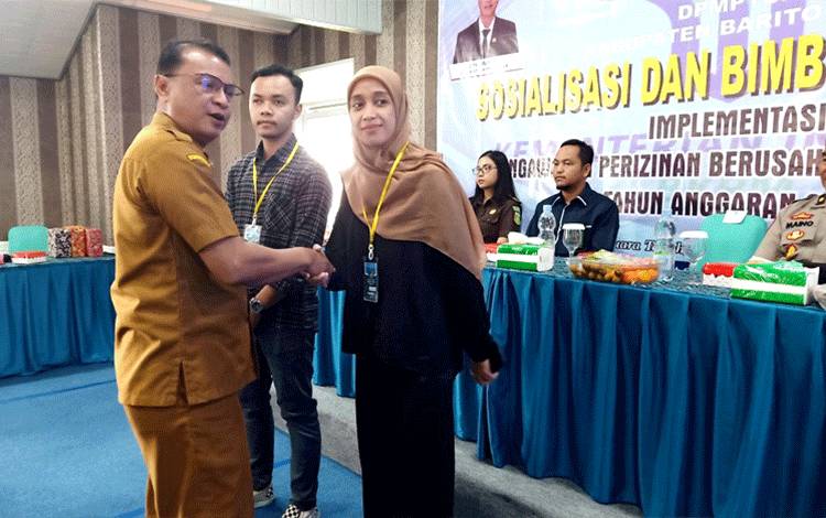 Plh Sekda Barito Utara, Drs Jufriansyah mengalungkan tanda peserta kepada dua perwakilan peserta sosialisasi dan bimtek implementasi pengawsan perizinan berusaha berbasis risiko, Senin 9 Oktober 2023 di aula salah satu hotel di Muara Teweh. (Foto: Dhani)