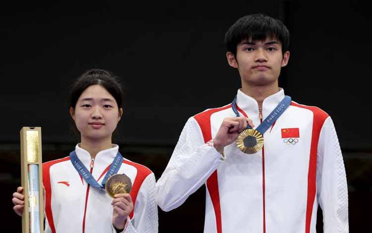 Huang Yuting dan Sheng Lihao berpose di podium kemenangan setelah mempersembahkan medali emas pertama untuk China dari Olimpiade Paris 2024 yang juga medali emas pertama Olimpiade ini, setelah menjuarai nomor menembak air rifle 10m beregu campuran di Chateauroux Shooting Centre, Prancis, 27 Juli 2024. (AFP/ALAIN JOCARD)