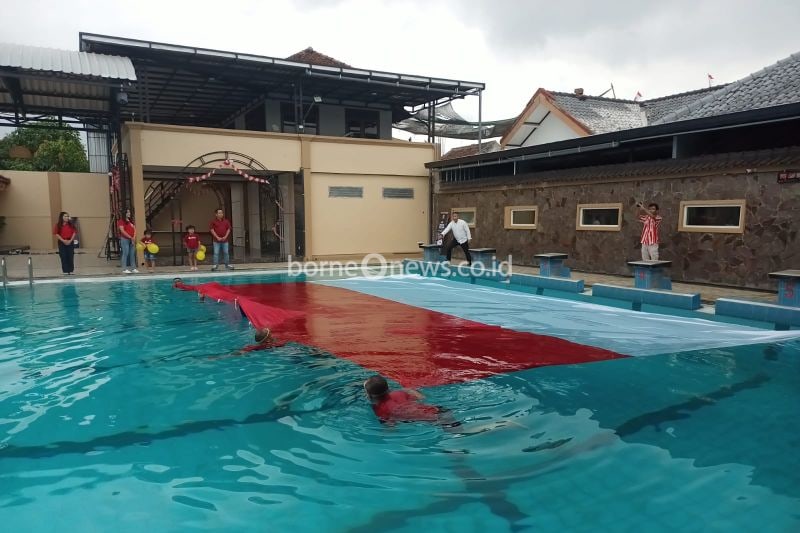 Sejumlah perenang membentangkan bendera merah putih raksasa di atas permukaan Kolam Renang Aquatic, Tulungagung, Sabtu (17/8/2024) (ANTARA/HO - Joko Pramono)