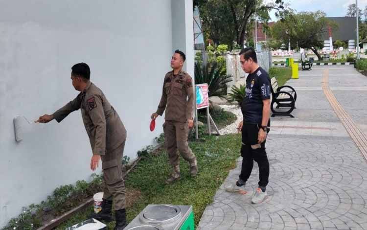 Anggota Satpol PP Mengecat kembali gedung di Bundaran Besar yang dicoret orang tidak dikenal. (FOTO: HENGKI)