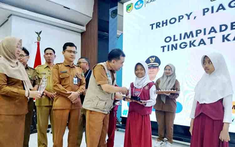 Kadis Pendidikan Barito Utara, Syahmiludin A Surapati didampingi Kabid Pembinaan Pendidikan Dasar, Samsul Astorijaya menyerahkan piagam dan tropi kepada para pelajar tingkat SD/MI pemenang OSN tingkat Kabupaten Barito Utara tahun 2025, di gedung balai Antang, Selasa 9 September 2025. (Foto: Dhani)
