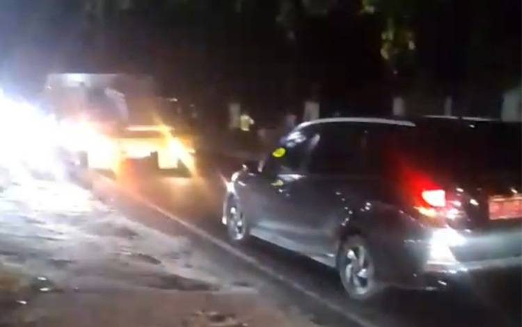 Beberapa kendaraan melambat akibat adanya pengendara yang mengalami kecelakaan akibat licinnya jalan di ruas Jalan Tjilik Riwut Km 36, wilayah Tangkiling, Kecamatan Bukit Batu pada Sabtu malam, 22 November 2025. (FOTO: Haris)