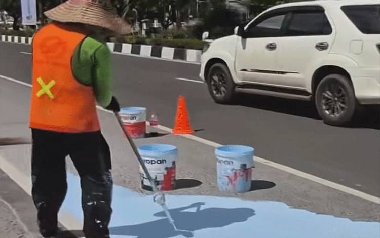 Petugas sedang menggunakan rol cat biru Jalan Imam Bonjol Palangka Raya berdekatan dengan Bundaran Besar. (Foto:MARINI)